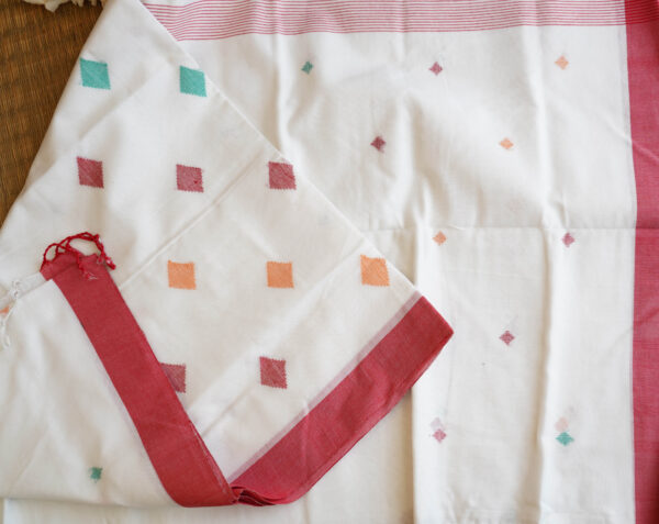 A pure cotton handwoven red and white Bengali Jamdani saree laid out on a mat, perfect for Durga Puja or Saraswati Puja